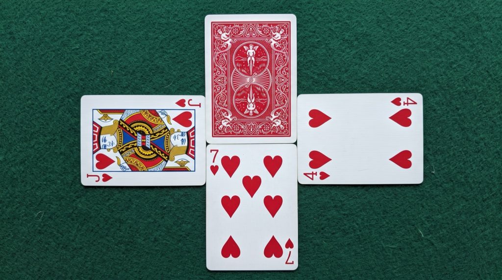 One cat te trick on green felt: seven of hearts led, jack of hearts and four of hearts played, and one card folded face down