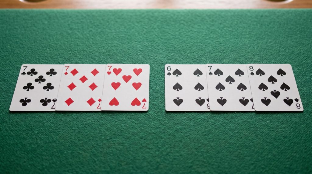 Two phom melds on green felt: three sevens of different suits, and the six, seven and eight of spades